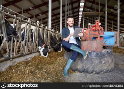 agriculture industry, farming, people, technology and animal husbandry concept - young man or farmer with tablet pc computer and cows in cowshed on dairy farm