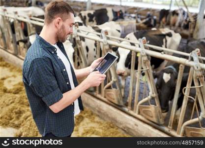 agriculture industry, farming, people, technology and animal husbandry concept - young man or farmer with tablet pc computer and cows in cowshed on dairy farm