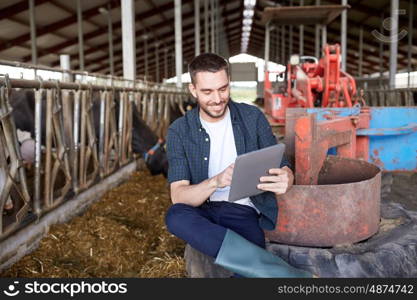 agriculture industry, farming, people, technology and animal husbandry concept - young man or farmer with tablet pc computer and cows in cowshed on dairy farm