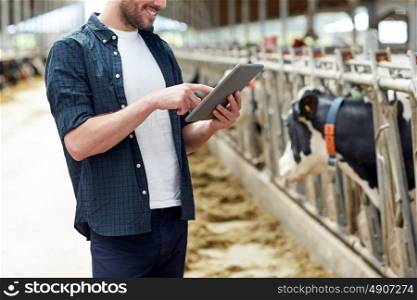 agriculture industry, farming, people, technology and animal husbandry concept - young man or farmer with tablet pc computer and cows in cowshed on dairy farm. young man with tablet pc and cows on dairy farm