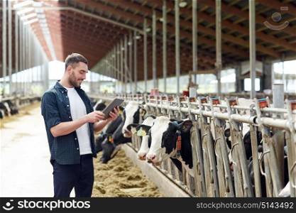 agriculture industry, farming, people, technology and animal husbandry concept - young man or farmer with tablet pc computer and cows in cowshed on dairy farm. young man with tablet pc and cows on dairy farm