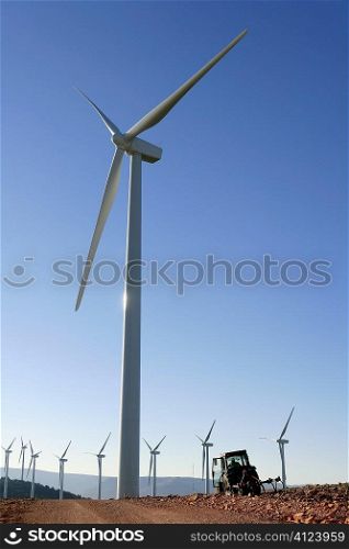 Agriculture tractor under electric wind mills in blue sky background