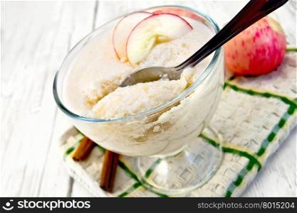 Air apple jelly in a glass bowl with a spoon, red apples and cinnamon on a towel on the background of wooden boards