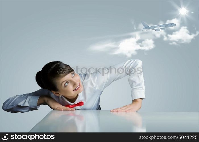 Air hostess. Young woman leaning above table and looking at airplane in sky