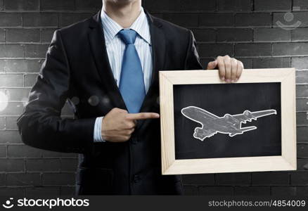 Air transportation. Close up of businessman holding wooden frame with airplane sign