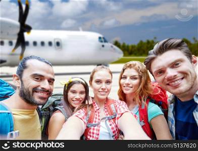 air travel, tourism and people concept - group of smiling friends with backpacks taking selfie over plane background. friends with backpack taking selfie over plane. friends with backpack taking selfie over plane