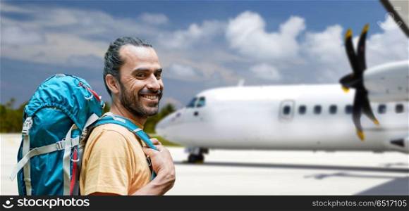 air travel, tourism and trip concept - smiling tourist man with backpack over plane on airfield background. tourist man with backpack traveling by plane. tourist man with backpack traveling by plane