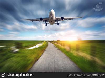 Aircraft and rural road with motion blur effect. Landscape with passenger airplane is flying over the asphalt road against cloudy sky, green grass field. Journey. Passenger airplane. Commercial plane
