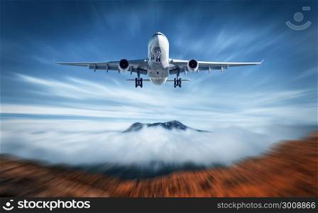 Aircraft mith motion blur effect is flying over low clouds. Landscape with passenger airplane, blurred clouds, mountains, blue sky. Passenger airplane. Business travel. Commercial plane. Concept