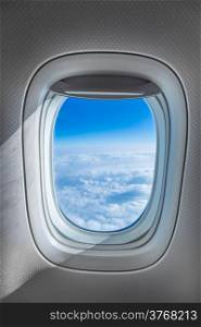 Aircraft Window with plane cruising against bright blue sky and clouds
