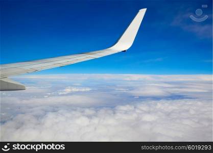 Aircraft wing flying into a blue sky and clouds