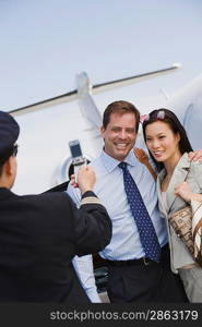 Airline pilot taking picture of businesswoman and businessman with mobile phone.