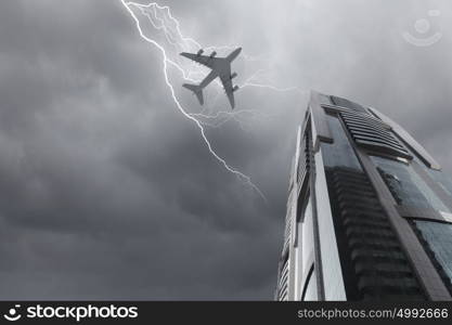 Airplane above city. Bottom view of airplane flying above skyscraper in stormy sky