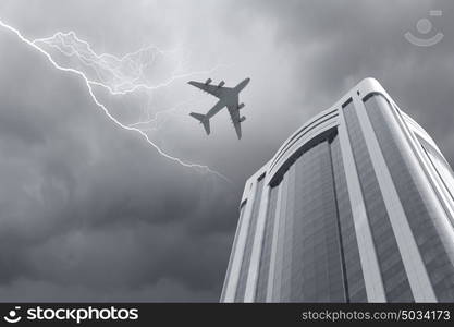 Airplane above city. Bottom view of airplane flying above skyscraper in stormy sky