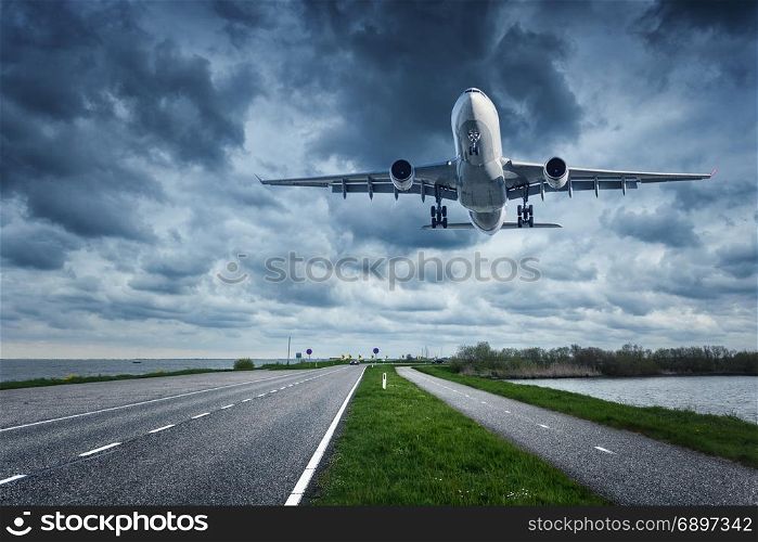 Airplane and road in overcast day. Landscape with big passenger airplane is flying in the cloudy sky over the asphalt road and grass. Passenger airliner is landing on the runway. Commercial plane