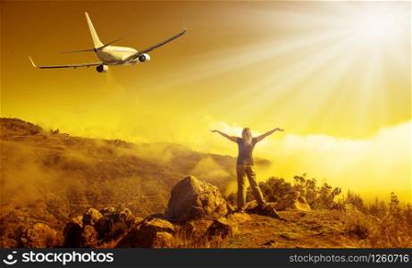 Airplane and woman at sunset. Summer landscape with girl standing on the mauntain with raised up arms and flying passenger airplane.