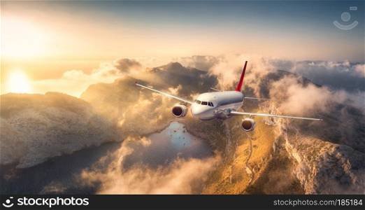 Airplane flying above mountains and low clouds at sunset in Spain. Landscape with passenger aircraft, cloudy sky, rocks, forest and sunlight. Business travel in commercial plane. Aerial view. Journey