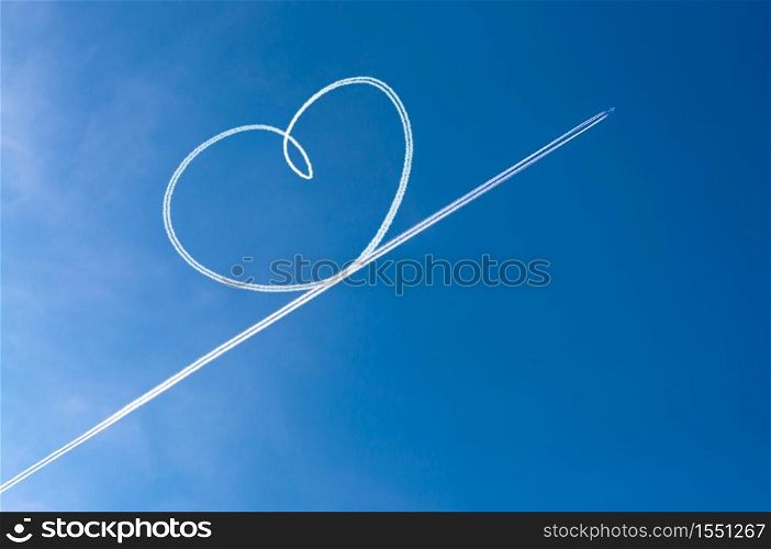 Airplane flying through clear blue sky left heart shape of vapour trails behide. Heart shapes on the sky from the planes traces.