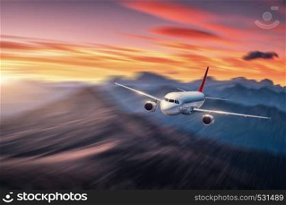 Airplane in motion. Aircraft with motion blur effect is flying over hills and mountains at sunset. Passenger airplane, blurred clouds. Passenger aircraft in motion. Business travel. Commercial.Concept