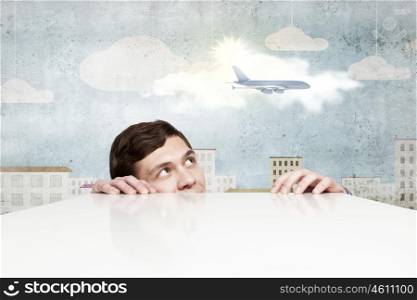 Airplane in sky. Young man looking from under table at flying airplane