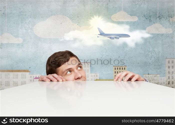 Airplane in sky. Young man looking from under table at flying airplane