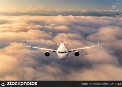 Airplane is flying above the clouds at sunrise in summer. Landscape with passenger airplane, beautiful clouds, mountains, sky. Aircraft is taking off. Business travel. Commercial plane. Aerial view