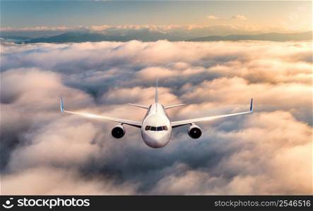 Airplane is flying above the clouds at sunrise in summer. Landscape with passenger airplane, beautiful clouds, sky. Aircraft is taking off. Business travel. Commercial plane. Aerial view. Front view