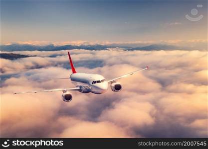 Airplane is flying above the clouds at sunset in summer. Landscape with passenger airplane, beautiful clouds, mountains, sky. Aircraft is taking off. Business travel. Commercial plane. Transport