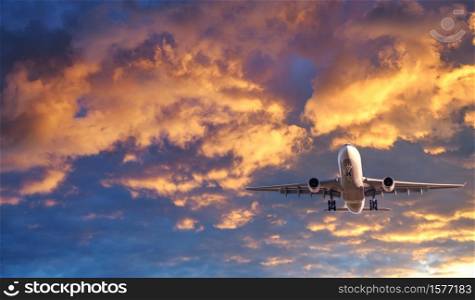 Airplane is flying in colorful sky at sunset. Landscape with white passenger airplane, purple sky with pink clouds. Aircraft takes off. Business trip. Commercial plane. Travel. Aerial view. Concept