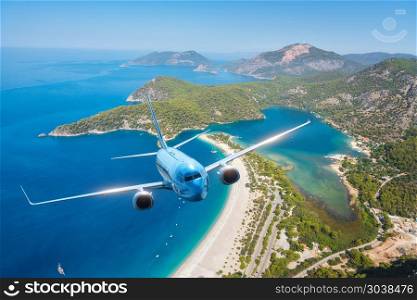 Airplane is flying over islands and sea at sunrise in summer. Landscape with white passenger airplane, seashore, mountains, sky, and blue water. Blue passenger aircraft. Travel and resort. Tourism. Blue airplane is flying over islands and sea at sunrise in summer