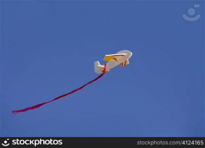Airplane kite flying on blue sunny sky with red tail