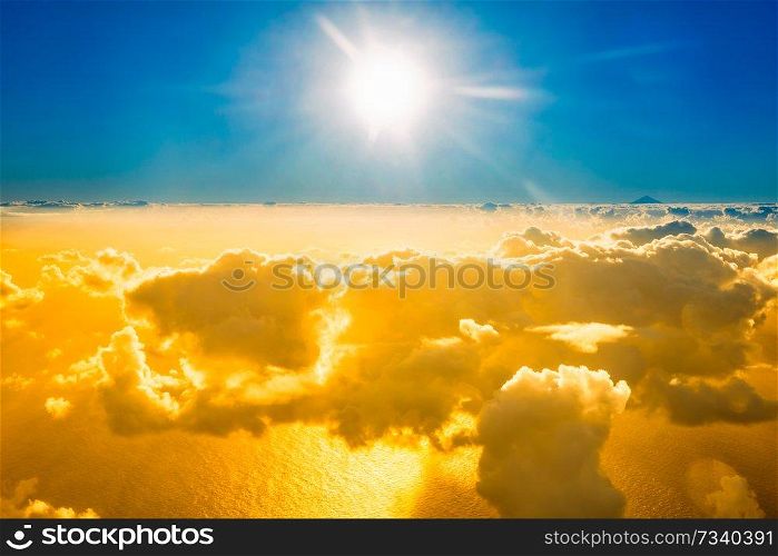 Airplane view of beautiful landscape with gold colored clouds, ocean with mountain peak and bright sunset shining sun