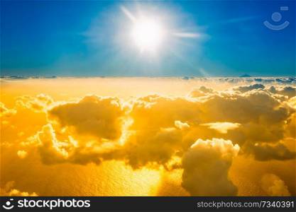 Airplane view of beautiful landscape with gold colored clouds, ocean with mountain peak and bright sunset shining sun
