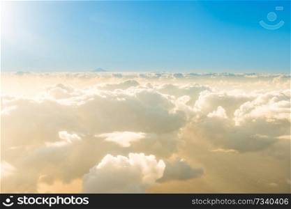 Airplane view of beautiful landscape with gold colored clouds, ocean with mountain peak and bright shining sun