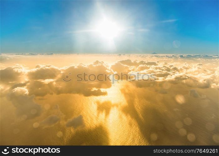 Airplane view of beautiful landscape with gold colored clouds, ocean with mountain peak and bright shining sun