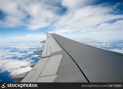 Airplane wing in the blue sky with white clouds