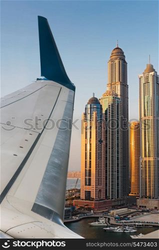 Airplane wing in the blue sky with white clouds. Dubai Marina at Dusk from the top