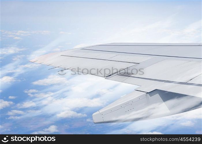 Airplane wing out of window. Flying airplane viewed from illuminator in blue sky