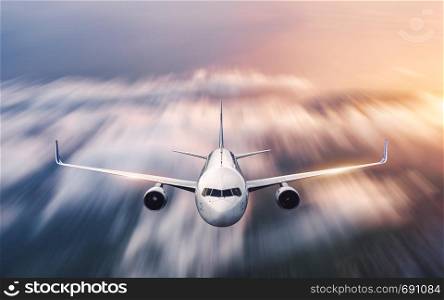 Airplane with motion blur effect is flying over low clouds at sunset. Passenger airplane, blurred clouds, colorful sky at dusk. Aerial view of the modern aircraft. Business travel. Commercial plane