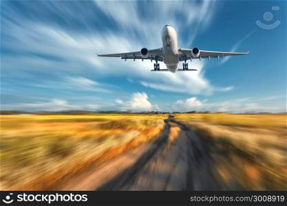 Airplane with motion blur effect. Landscape with flying passenger airplane and blurred blue sky with clouds, orange grass field with trail at sunset. Passenger airplane is landing. Commercial aircraft