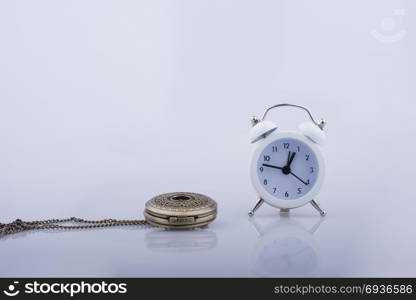 Alarm clock and a pocket watch side by side on white background