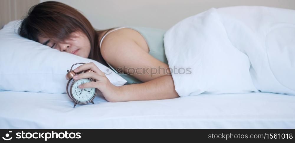 alarm clock and asian woman hand stop time in bed while sleeping, young adult female wake up late in the morning. fresh relax, sleepy and have a nice day concepts