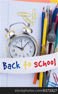 alarm clock and school supplies close up with back to school text on paper ribbon. back to school