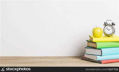 Alarm clock and yellow apple on stack of books