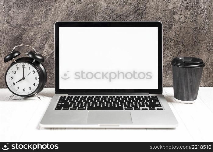 alarm clock disposable coffee cup with open laptop white desk