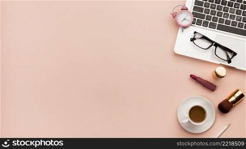 alarm clock eyeglasses laptop with coffee cup makeup product against peach backdrop