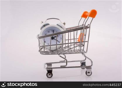 Alarm clock in a shopping trolley on white background