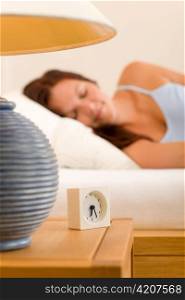 Alarm clock on bedside table woman sleeping in white bed