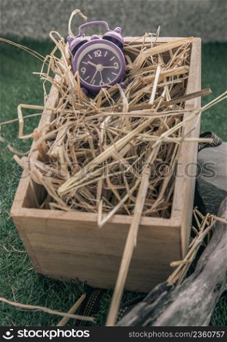Alarm clock on straw background in wooden box. Gift concept of beginning for new day, Selective focus.