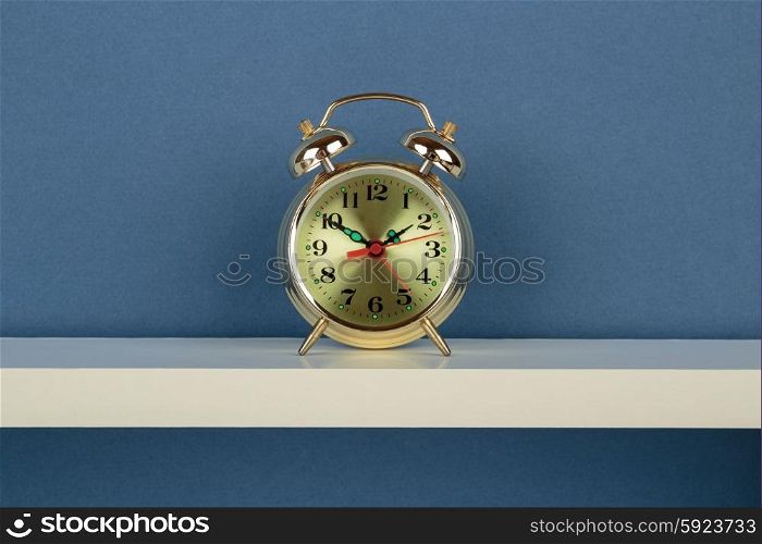 Alarm clock on white shelf on blue wallpaper background